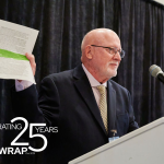 Man stands at podium and holds a pile of papers in the air