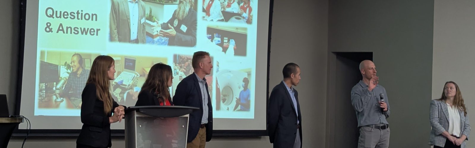 Six people stand in front of a projector screen